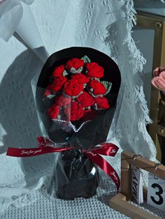 a bouquet of red roses in a black paper wrapper next to a small wooden box