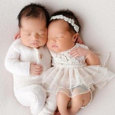 two babies are laying next to each other on a white surface, one is holding the baby's head