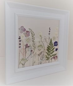 a white frame with flowers and leaves on it in front of a wall mounted art piece