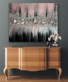 an abstract painting hangs on the wall above a dresser with flowers and vases in it