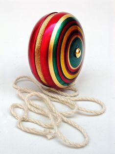 a red, yellow and green striped ball with string on white surface next to twine