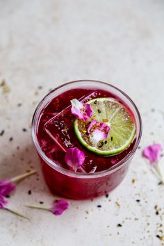 a drink in a glass with a slice of lime and flower on the rim next to it