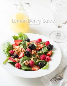 a white plate topped with berries and spinach next to a glass of orange juice