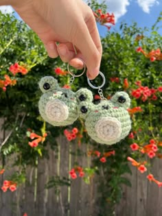 two crocheted frog keychains being held by a person's hand