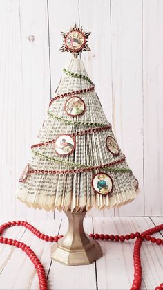 a christmas tree made out of old book pages on a white wooden table with red beads