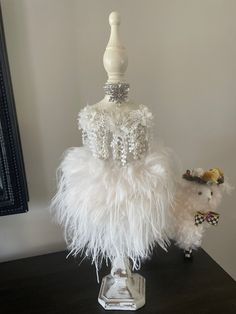 a white mannequin with feathers on it and a small stuffed animal next to it