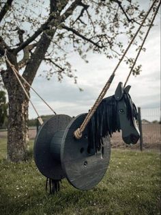 a horse that is hanging from a rope attached to a tree branch in the grass