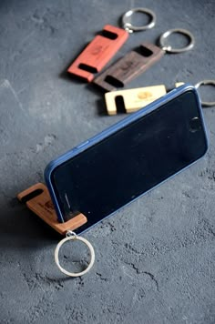 three wooden keychains are attached to a cell phone with two metal rings hanging from them