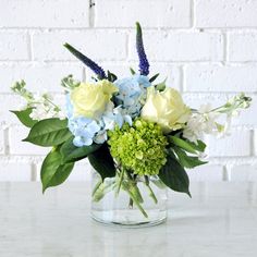 a vase filled with blue and white flowers on top of a marble counter next to a brick wall