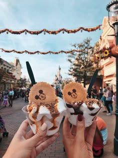 two ice cream sundaes with mickey mouse faces on them are being held up in front of the camera