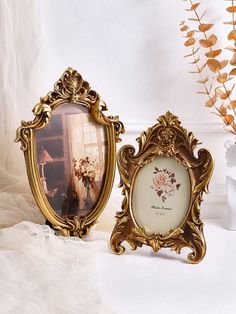 two ornate gold frames sitting next to each other on a white table with flowers in the background