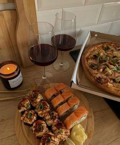 two pizzas and some appetizers are sitting on a table with wine glasses