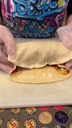 a person in white gloves holding a tortilla on top of a counter