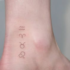 a small tattoo on the foot of a woman's ankle that has three zodiac symbols