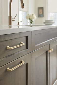 a kitchen with gray cabinets and brass pulls on the handles, along with white flowers