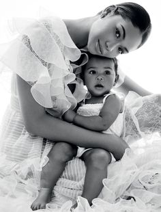 a woman holding a baby in her arms while posing for a black and white photo