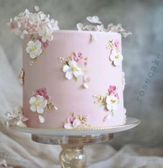 a pink cake with white flowers on it sitting on top of a metal platter