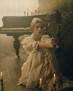 a woman sitting on the floor next to a piano with candles in front of her