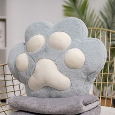 a blue and white dog paw pillow sitting on top of a chair next to a plant