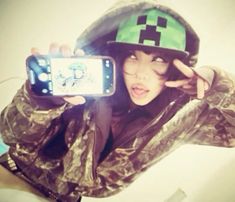 a woman taking a selfie with her cell phone wearing a green hat and camo jacket