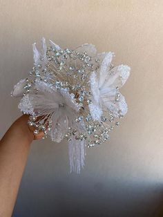 a hand holding a white flower with lots of crystals on it's petals and attached to the ceiling