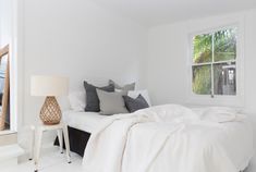 a bed with white sheets and pillows next to a window in a room filled with furniture