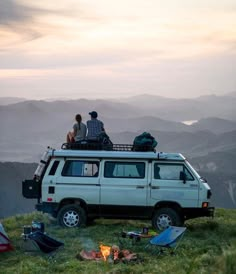 two people sitting on top of a van in the mountains with their campervan