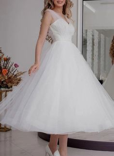 a woman in a white dress is standing near a mirror and posing for the camera