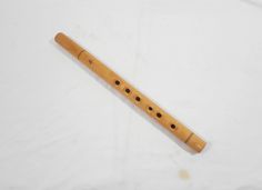 a wooden flute with holes in the middle on a white sheeted surface and one piece of wood sticking out of it's side