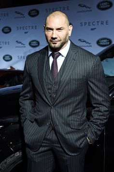 a bald man in a suit and tie standing next to a black car at an event