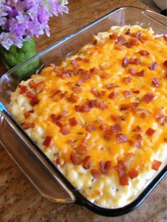 a casserole dish with cheese and bacon in it sitting on a table next to purple flowers