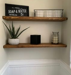 two wooden shelves with plants and candles on them in the corner of a white bathroom