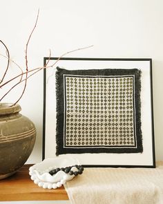 a black and white framed artwork next to a vase with dried branches in it on a wooden table