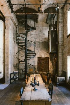 a long table with chairs and a spiral staircase in the middle of an old building