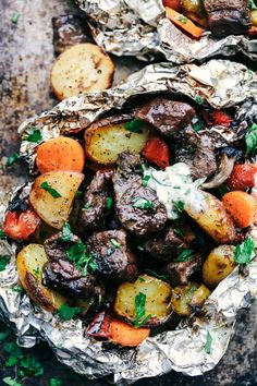 two foil packets filled with meat, potatoes and carrots on top of a table