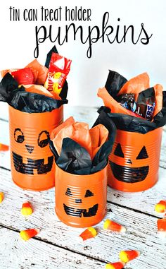 three tin can halloween treat holders with candy in them on a white wooden table and text overlay that says, tin can treat holder pumpkins