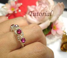 a woman's hand holding a ring with pink stones on it and flowers in the background