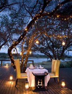 an outdoor dining area is lit up with candles and lights on the table, along with two chairs