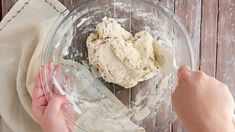 someone mixing dough in a glass bowl on top of a wooden table next to a napkin