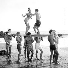 a group of men standing around each other on top of a surfboard at the beach