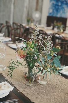 the table is set with place settings and flowers in vases on top of burlap