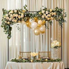 the table is set up with balloons and greenery for an elegant wedding reception in white and gold