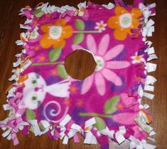 a pink and purple flowered cloth with white ruffles on the bottom, sitting on a wooden floor