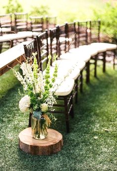 an arrangement of flowers and greenery sits on a wooden table in front of rows of chairs