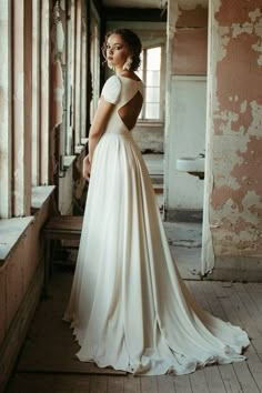 a woman is standing in an old building wearing a wedding dress and looking off into the distance