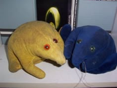 two stuffed animals sitting next to each other on a desk with books in the background