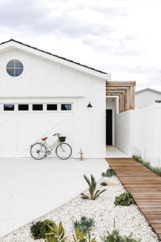 a bike is parked in front of a white house with a wooden walkway leading to it