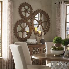 a dining room table with white chairs and two mirrors on the wall above it, along with potted plants