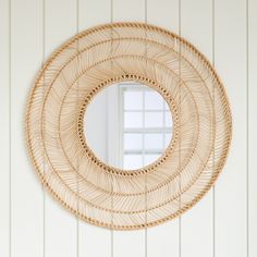 a round rattan mirror hanging on the wall next to a white wooden door with shutters