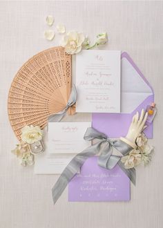 the wedding stationery is laid out on top of the table with flowers and fan